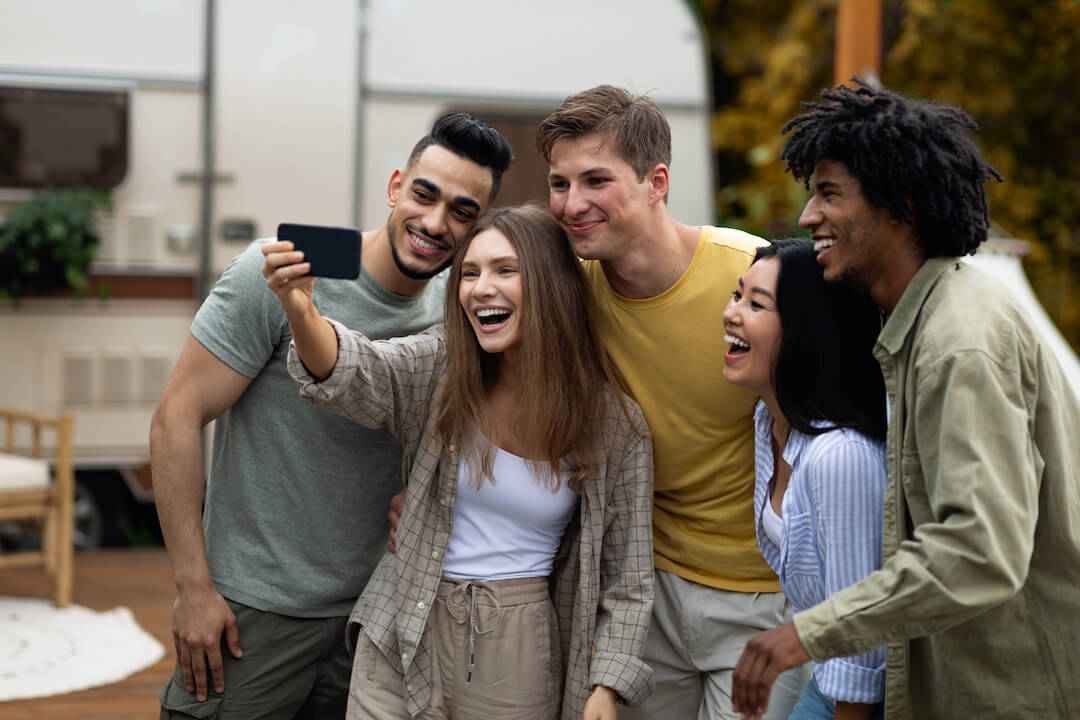 Un groupe d'amis prenant un selfie près de leur roulotte, souriant et s'amusant ensemble